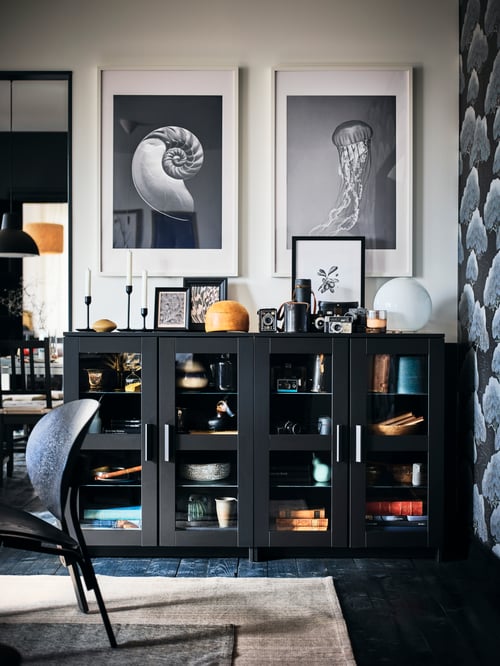 A dining area with side-by-side, black BRIMNES glass-door cabinets with decorative displays in, on and above them.