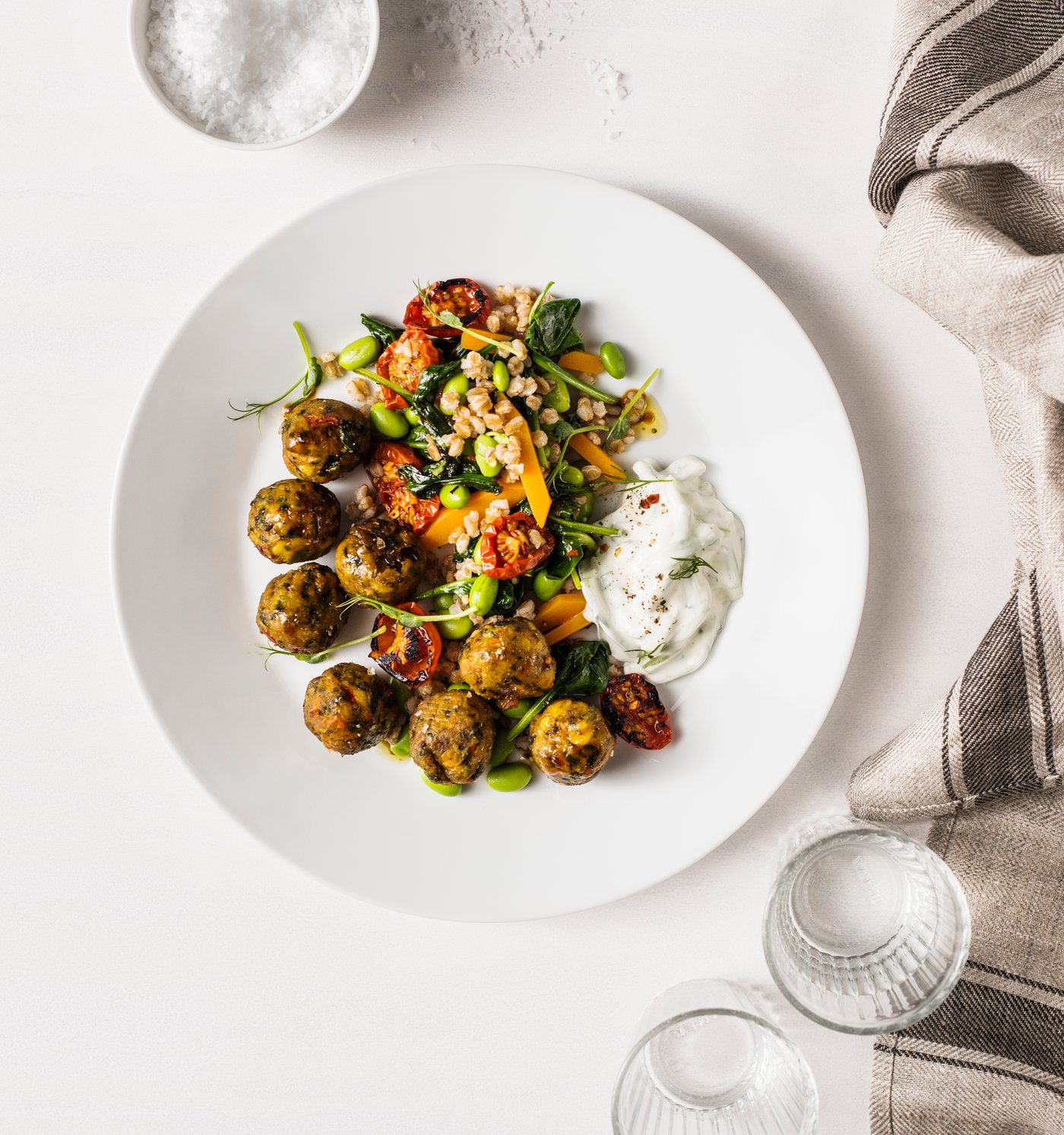Vista superior de un plato de albóndigas con acompañamiento sueco en un plato blanco sobre una mesa blanca.