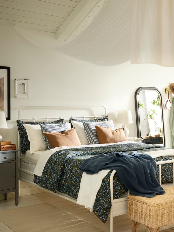 A white STJÄRNÖ bed covered in a ROSENTIBAST 3 comforter set and a white INDIRA NN bedspread and various cushions.