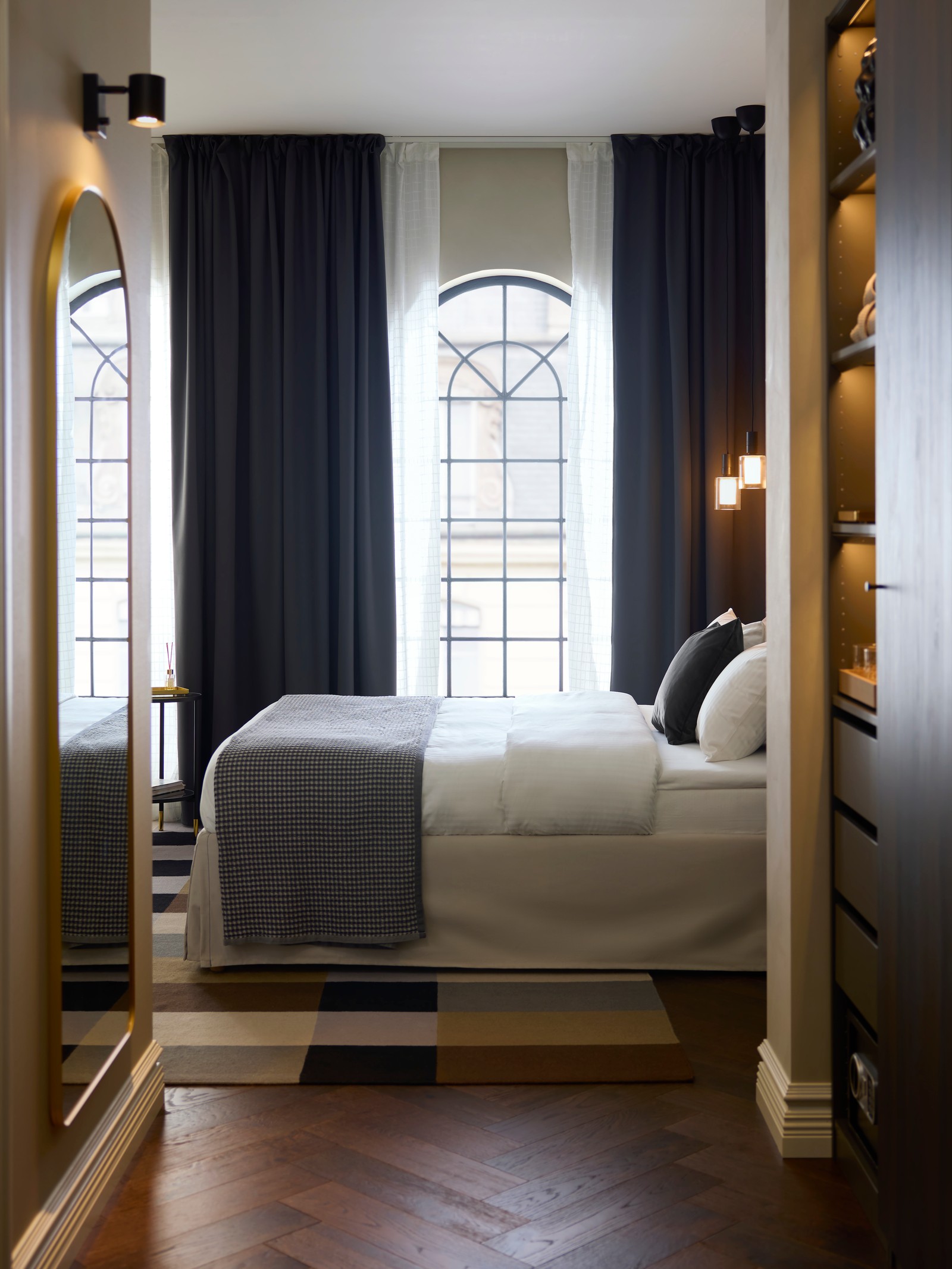 A person is in hotel room with tall windows, by a beige TÄRNKULLEN upholstered bed frame with a bed skirt.