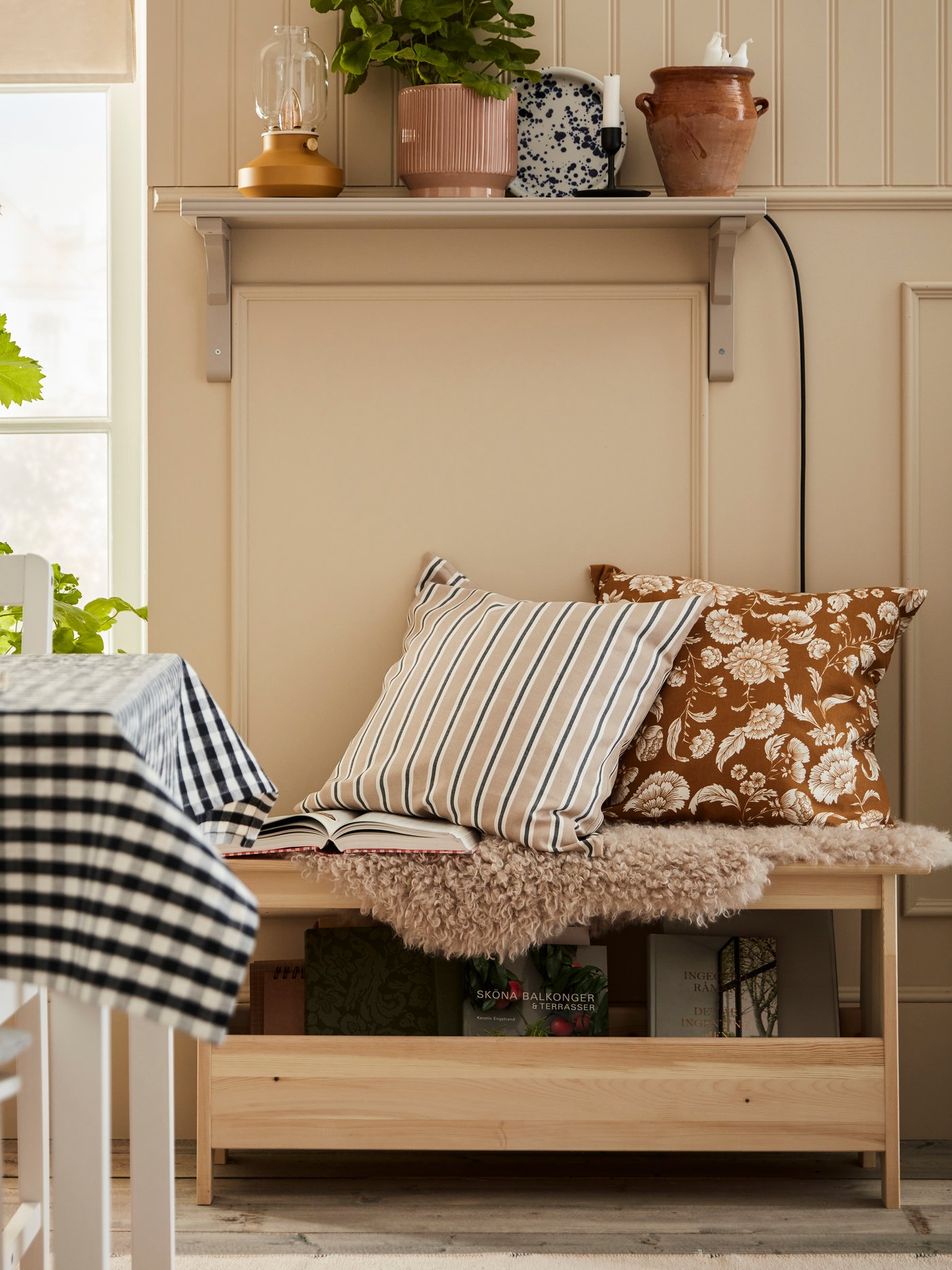 Een houten PERJOHAN bankje met opbergruimte en twee sierkussens erop in de woonkamer naast de eettafel.