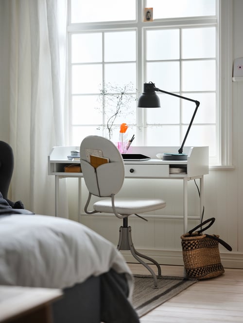 Un spațiu de lucru modern, care dispune de un birou dreptunghiular, un scaun rotativ bej, o lampă de lucru cu încărcare wireless și perdele.