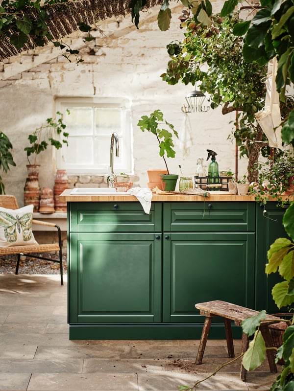 A green kitchen with a chrome INSJÖN tap and an abundance of real and artificial plants.