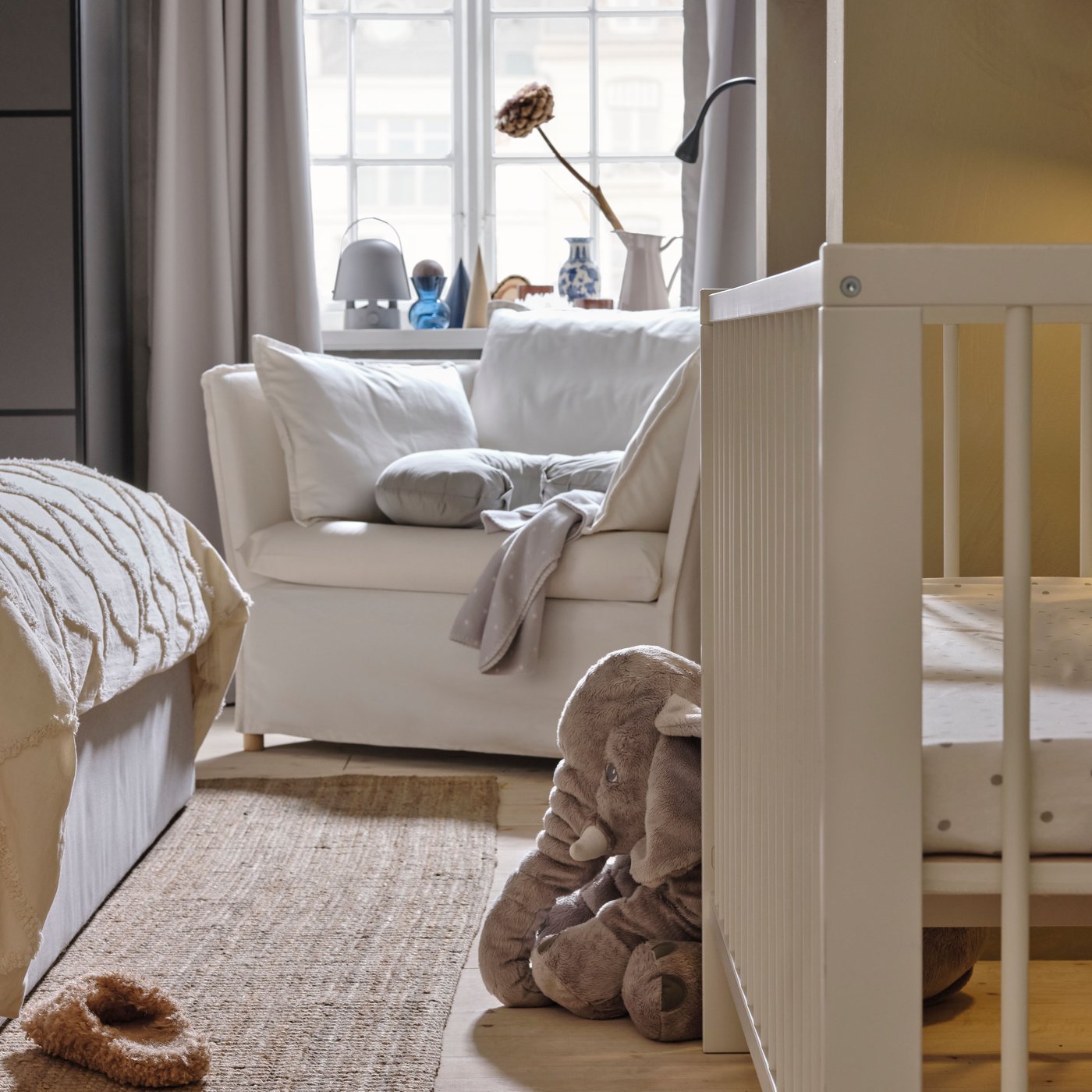 A white BACKSÄLEN 1.5 seat armchair in front of a window with a white GULLIVER cot and a soft toy elephant in front of it.