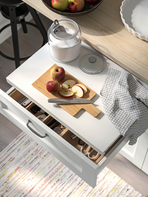 An UTRUSTA pull-out shelf has been pulled out in a drawer with a white ENKÖPING front and a chrome-plated ENERYDA handle.