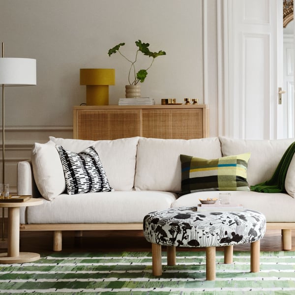 A living room with a STOCKHOLM 2025 3-seat sofa, pillows and a throw on it, and a black and white pouffe on a rug in front.