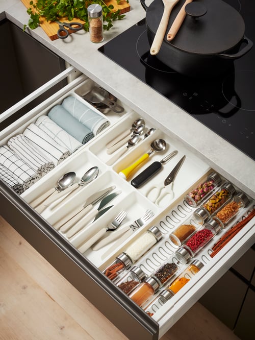 Kitchen drawer with cutlery, tea towels and spices placed in VARIERA spice-jar inserts and STÖDJA cutlery and utensil trays.