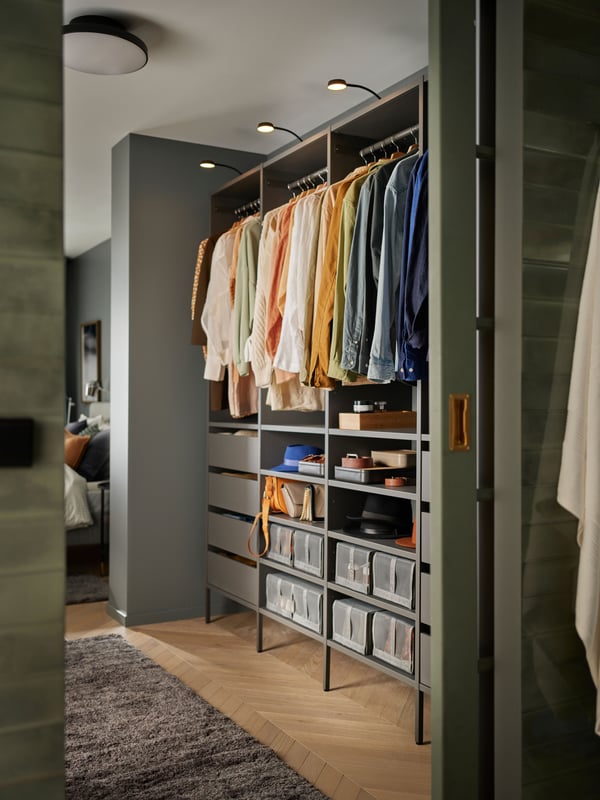 Combinaison armoire-penderie ouverte en gris foncé avec des tablettes, des tiroirs, des boîtes de rangement et des vêtements suspendus bien rangés.