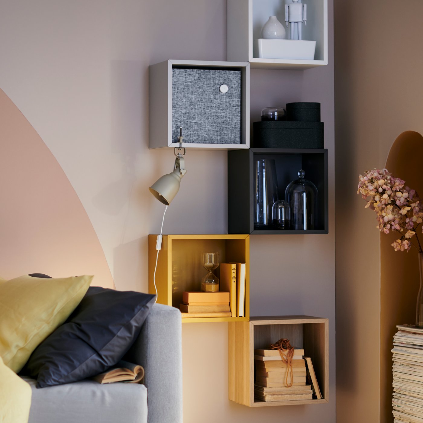 Moderne, offene Wandregale in verschiedenen Farben, dekoriert mit Büchern, Boxen, Glasvasen und einer Leseleuchte neben einem Sofa.