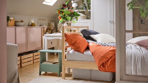 A rustic-style bedroom contains a white HAUGA extendable table by a pine TARVA bed covered in red-brown ÄNGSLILJA bed linen.