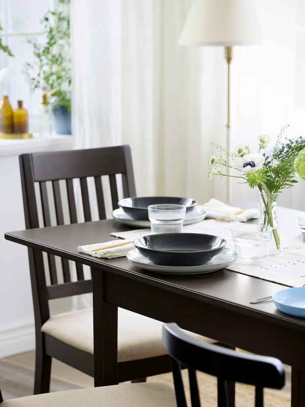Une salle à manger moderne avec une table et des chaises NÄSINGE en brun foncé, accompagnées de plantes décoratives.