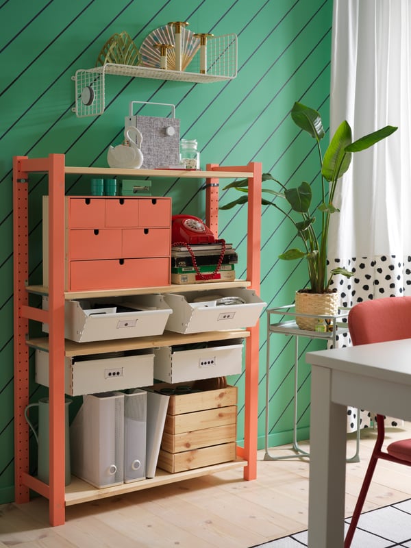 A dining room with IVAR shelving unit with white drawers, a white wall shelf, white curtains and a green plant stand.