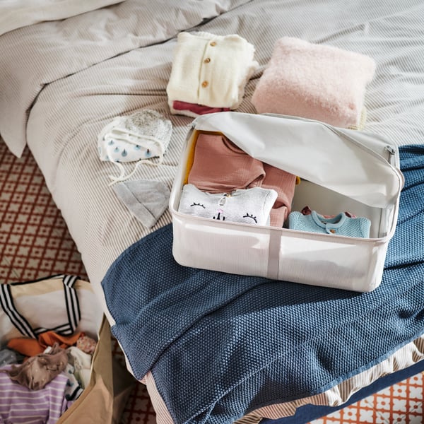 A bed covered in SOLFIBBLA bed linen and a HUMLEMOTT throw has a HEMMAFIXARE storage case on top holding folded clothes.