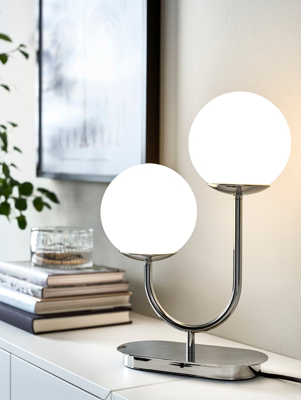 A grey-turquoise SNÖBYAR lamp is set on a VITTSJÖ nesting table beside a VIMLE sofa in a living room on a sunny day.