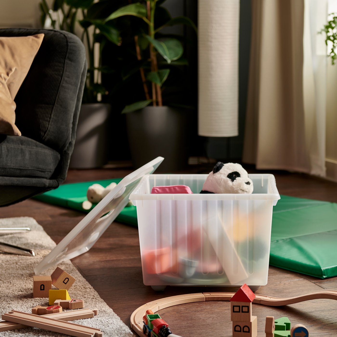 A softly sunlit living room featuring a white VESSLA storage crate with castors, surrounded by a sofa and toys.