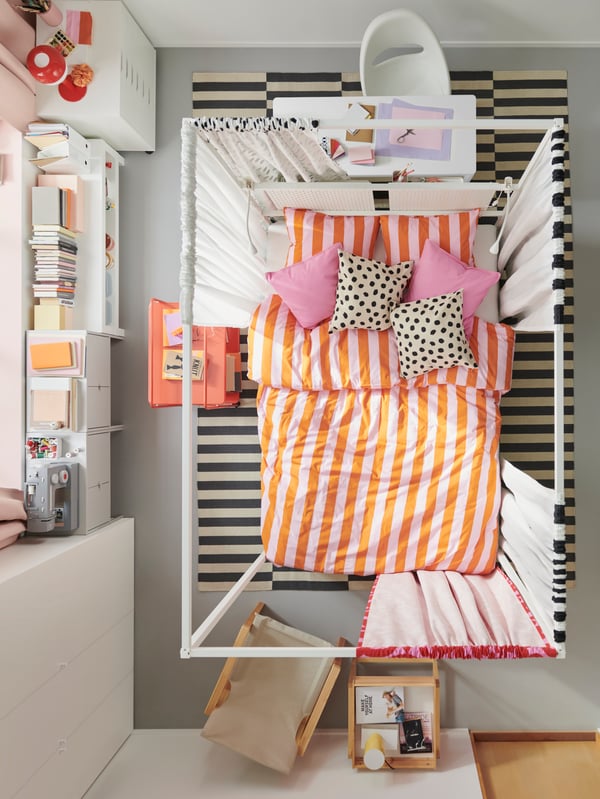An overhead view of a bedroom with a VITARNA four-poster bed in the middle with pink/orange SLÅNHÖSTMAL bed linen on it.