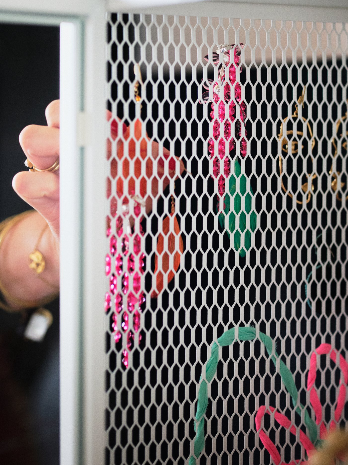 وحدة تخزين بسطح شبكي معدني أبيض رأسي. يد امرأة تعلق عدة أقراط في فتحات الشبكة.