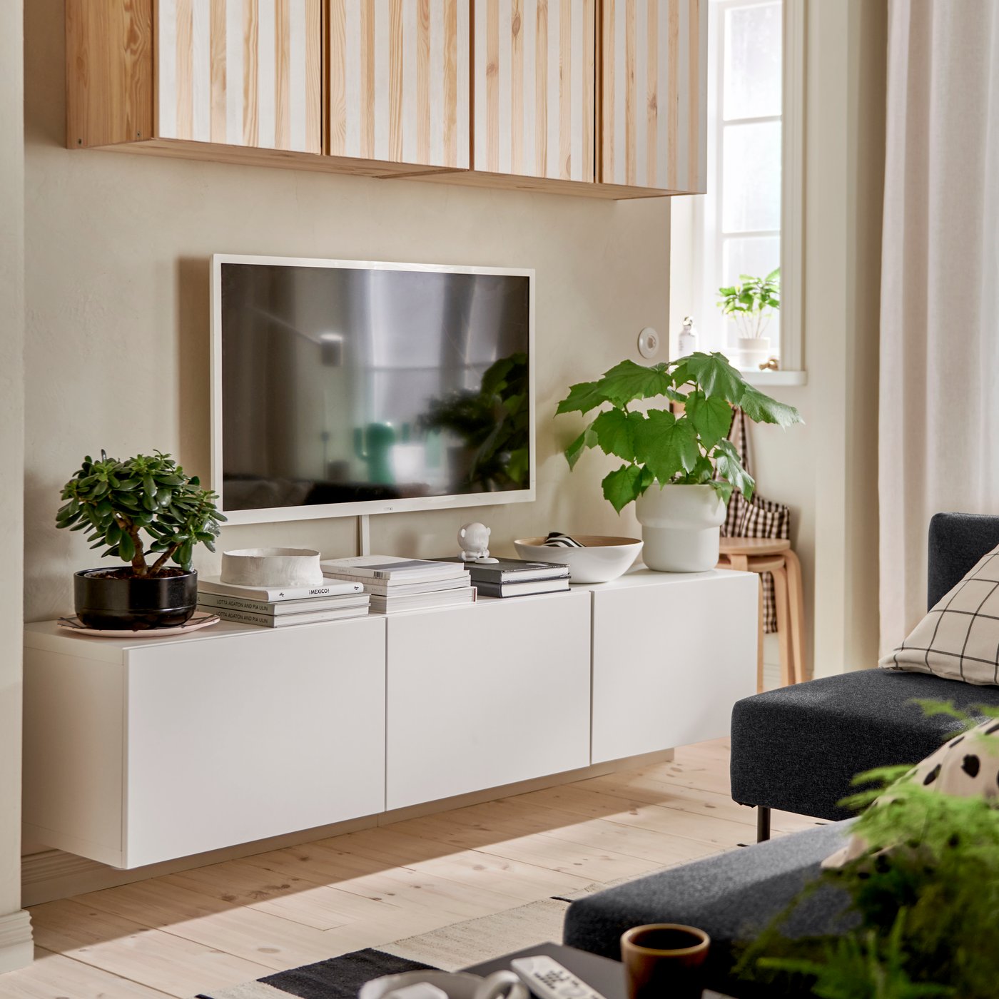 A white BESTÅ TV bench with doors is mounted on a wall underneath a wall-mounted TV and IVAR cabinets painted with stripes.