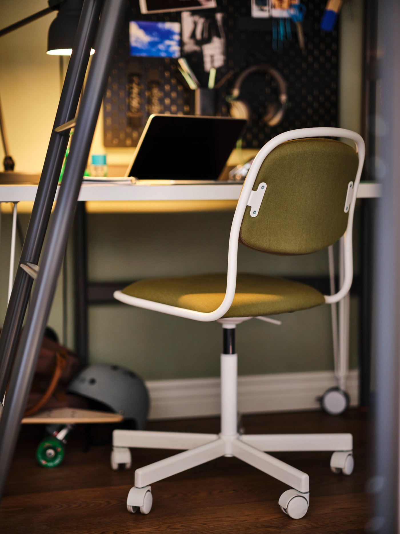 A yellow-green ÖRFJÄLL swivel chair in front of a desk with a laptop on top and a skateboard and helmet below.