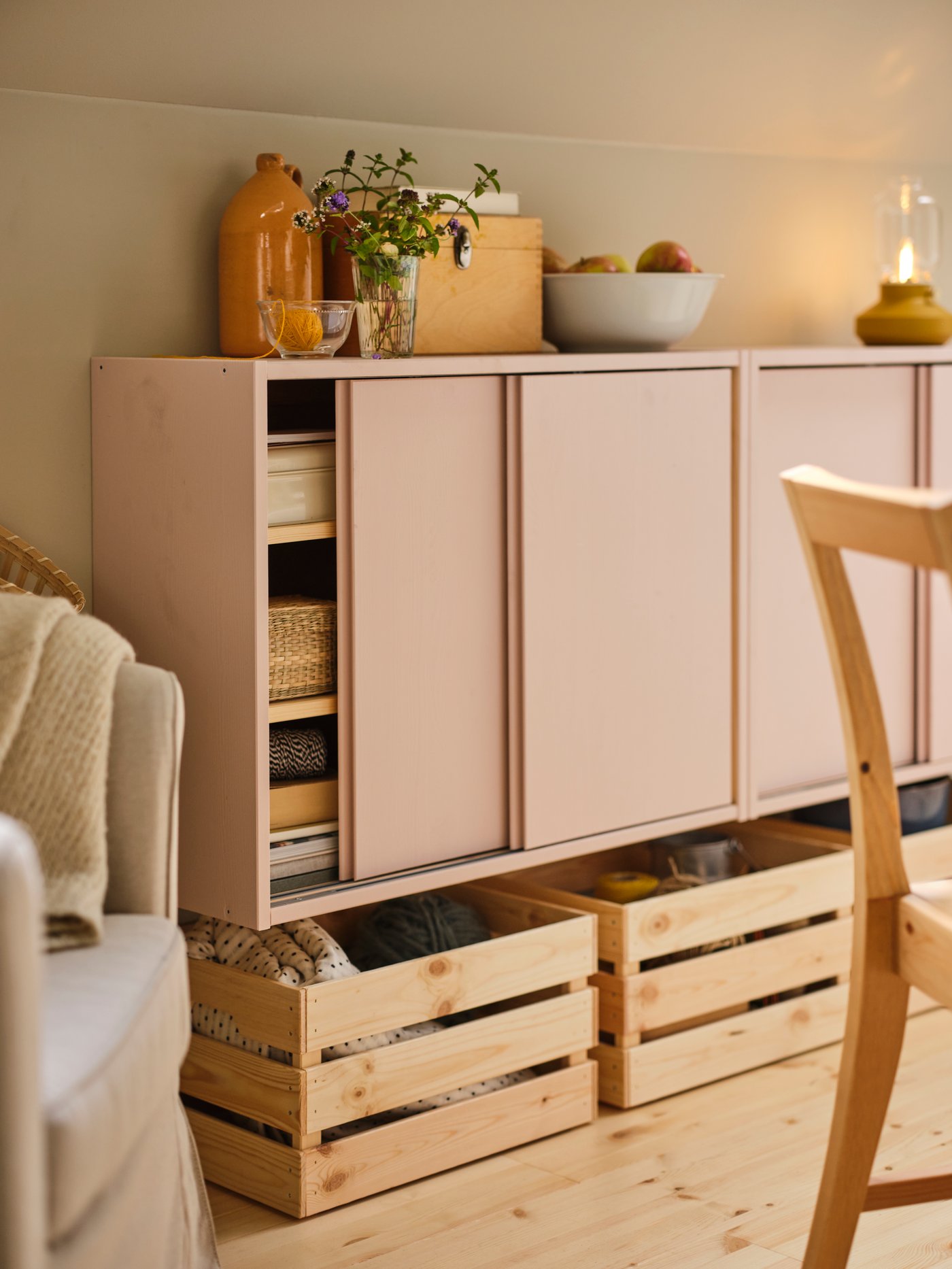 Two IVAR cabinets with sliding doors painted pink on a wall with a bowl and vases on top and three KNAGGLIG boxes underneath.