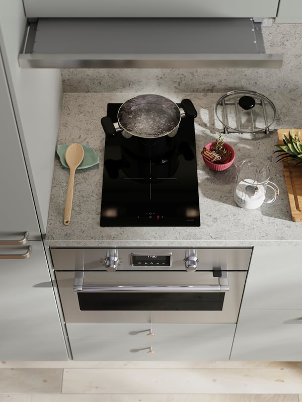 In una cucina con frontali HAVSTORP grigio chiaro, un piano cottura a induzione VÄLBILDAD e un forno termoventilato/vapore diretto FORNEBY.