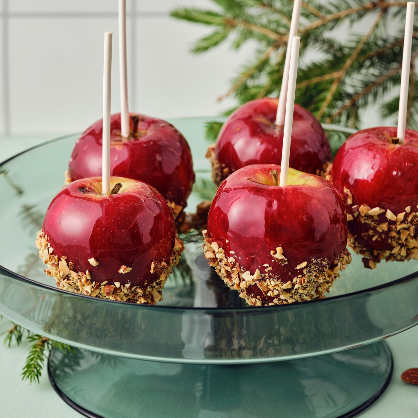Five candied apples on a green glass serving plate.