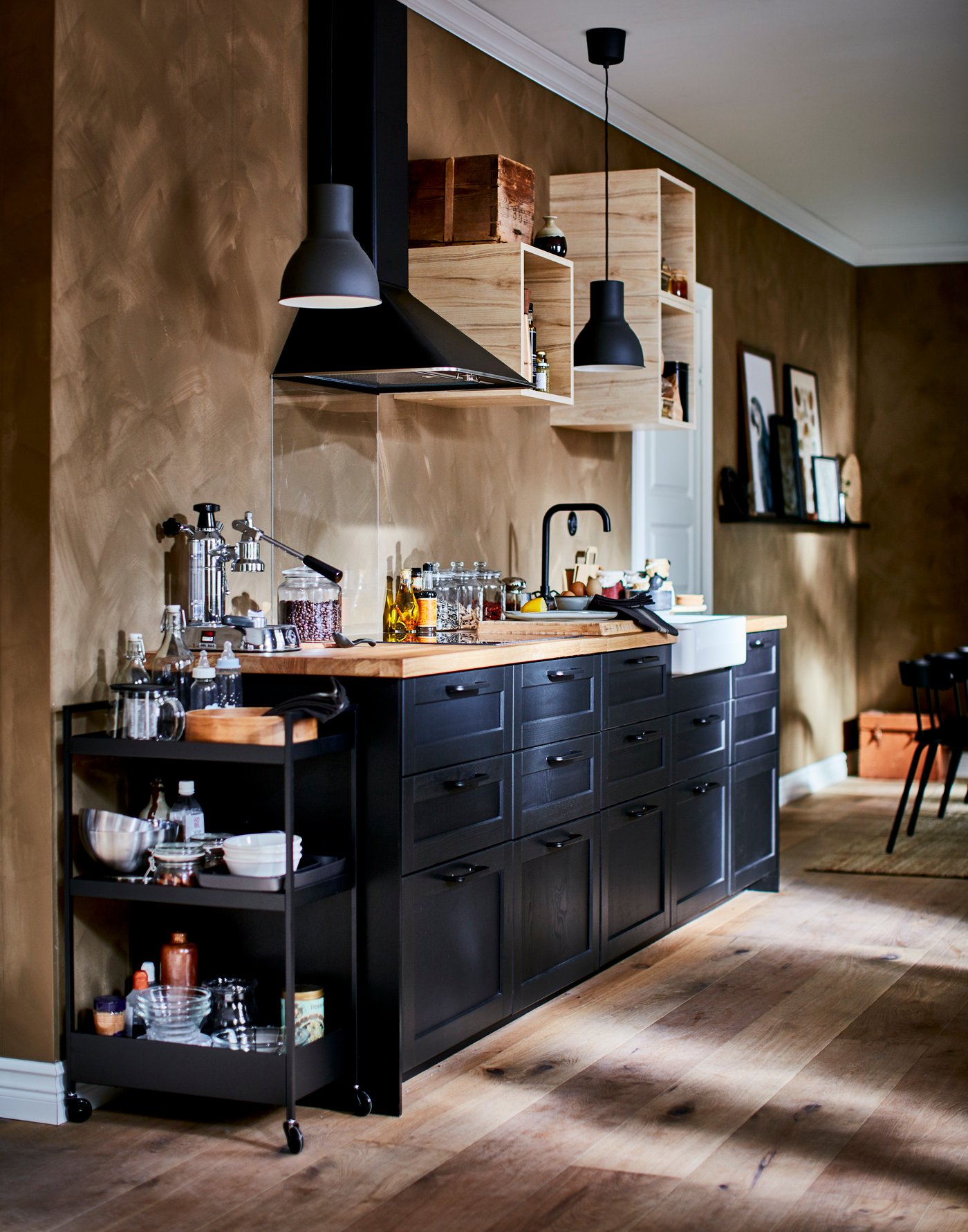 Schön ausgestattete Küchenzeile mit kleinen, offenen Wandschränken, einer Dunstabzugshaube, einem schwarzen Servierwagen und LERHYTTAN Schubladenfronten.