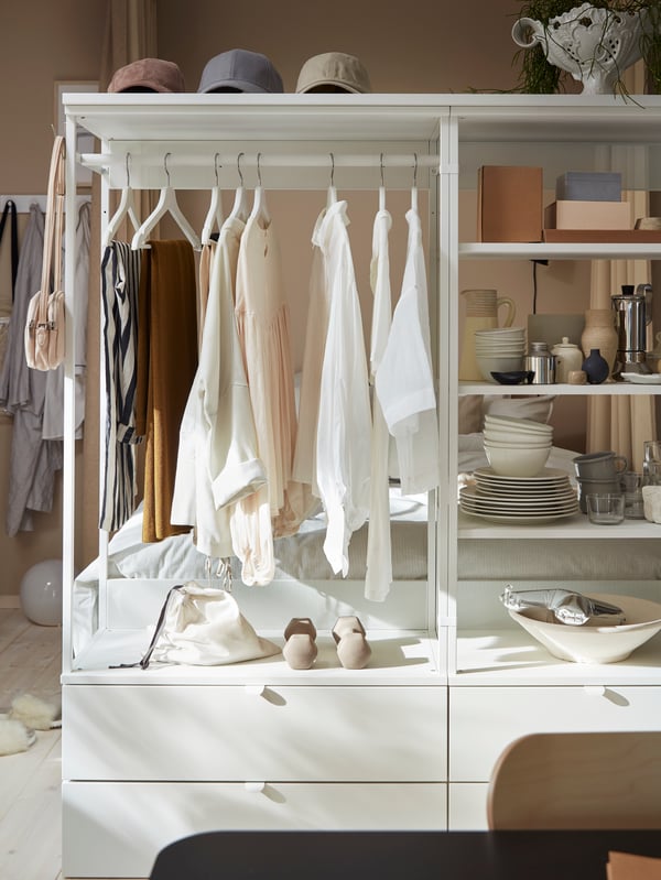 An open PLATSA wardrobe with drawers, shelves and a rail. Clothes hang on white hangers, and other items are on the shelves.