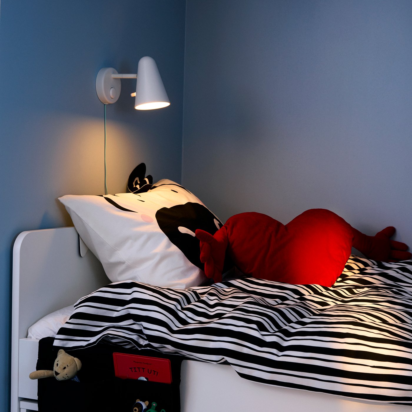 A corner with blue walls and SLÄKT bed with NATTHÄGER bedding with black/white zebra pattern and FAMNIG HJÄRTA cushion.
