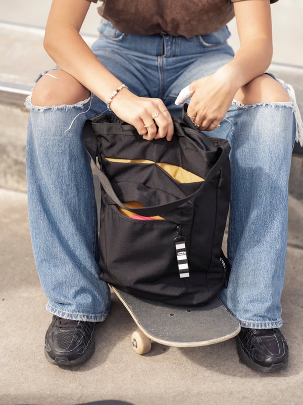 Mochila negra VÄRLDENS junto a pantalones.
