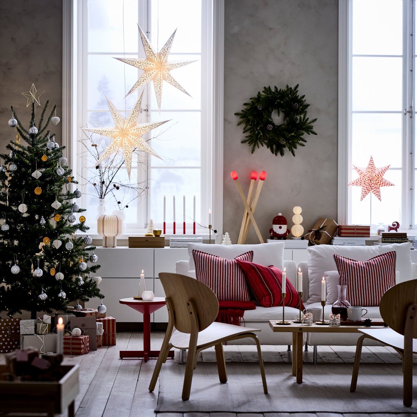 Ett mysigt julpyntat vardagsrum med höga fönster är dekorerat för jul med VINTERFINT dekorationer och STRÅLA adventsstjärnor.