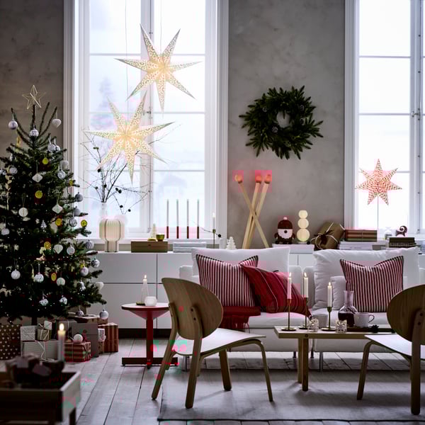 Ett mysigt julpyntat vardagsrum med höga fönster är dekorerat för jul med VINTERFINT dekorationer och STRÅLA adventsstjärnor.
