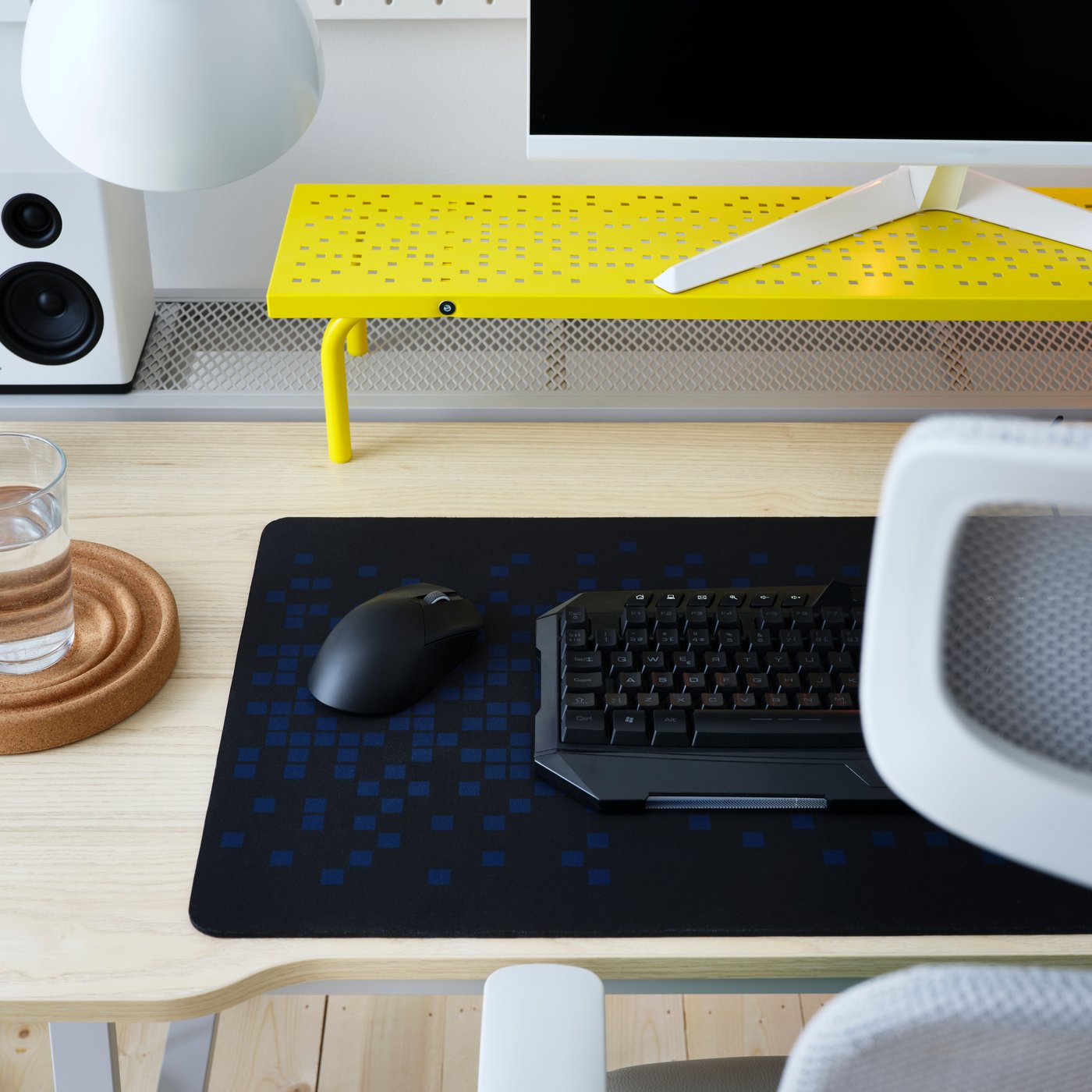 A keyboard, mouse, monitor and BRÄNNBOLL gaming mouse pad on an UTESPELARE desk with a yellow LÅNESPELARE monitor stand.