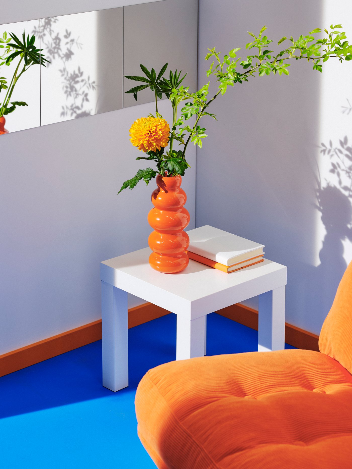 A white coffee table with an orange vase filled with flowers and an orange DYVLINGE swivel armchair.
