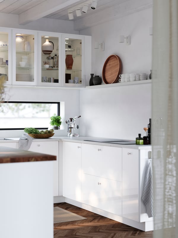 A bright kitchen with a wood floor has cabinets with glossy white RINGHULT fronts and wall cabinets with HEJSTA glass doors.