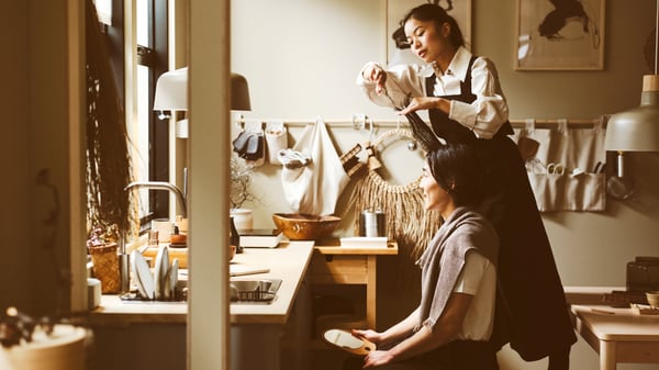 A standing person cutting the hair of a seated person in a kitchen with an ash effect EKBACKEN worktop.