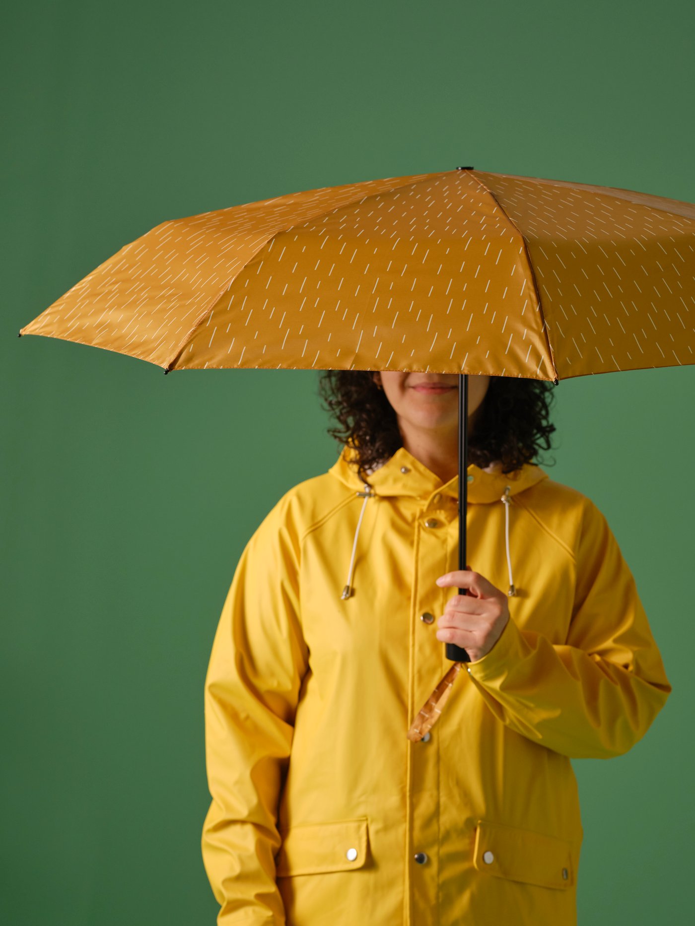 Oseba v eni roki drži KNALLA zložljiv dežnik. Odprt dežnik zakriva njen obraz.