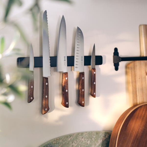 Five VARDAGEN knives with wooden handles, in various sizes, are displayed on a black magnetic rail mounted on a wall. 