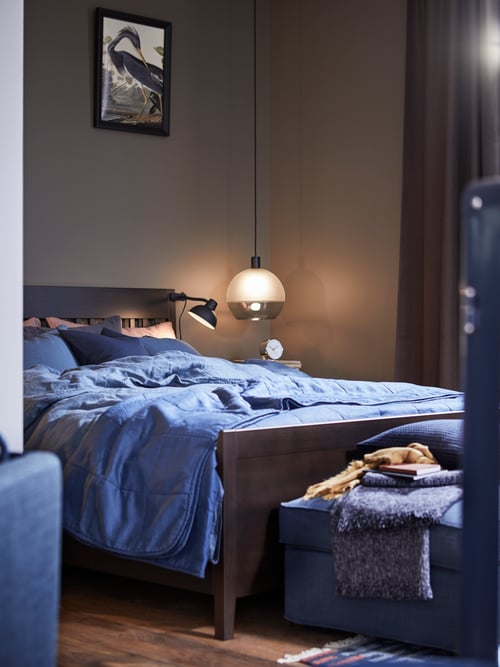 A bedroom featuring a bed frame with storage made of solid wood, covered with a blue duvet cover and pillowcase.