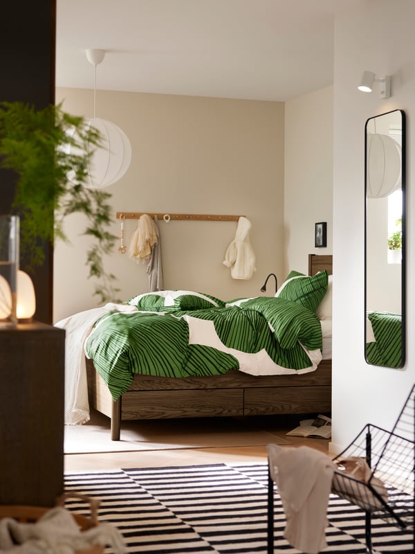 The entrance to a bedroom with TONSTAD bed made up with KUNGSCISSUS bedding in green/white. STOCKHOLM rug on the floor.