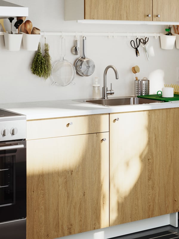 A stylish KNOXHULT base cabinet in light wood with a drawer and doors, set in a modern kitchen with white tiles.