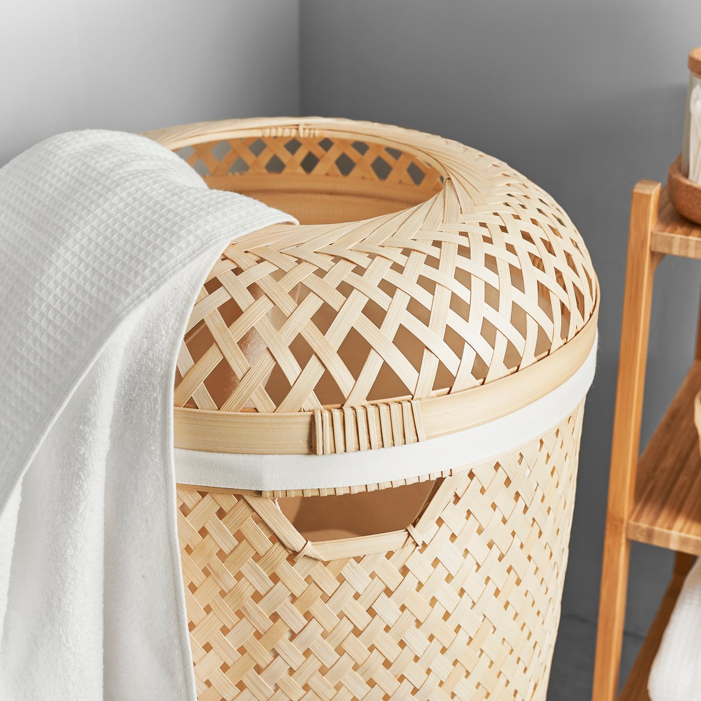 SALUDING laundry basket with a white towel hanging over the top. Beside it is a bamboo shelving unit.