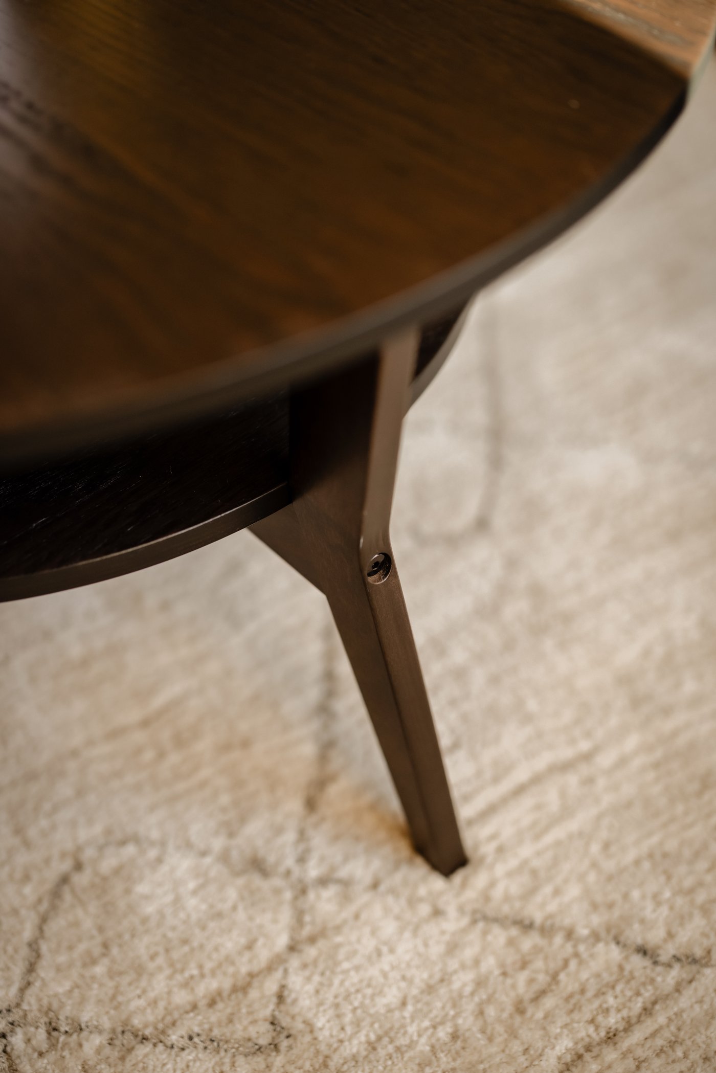 Close-up van een ronde, donkerbruine JAKOBSFORS salontafel in eiken fineer. Hieronder ligt een TVERSTED beige vloerkleed.