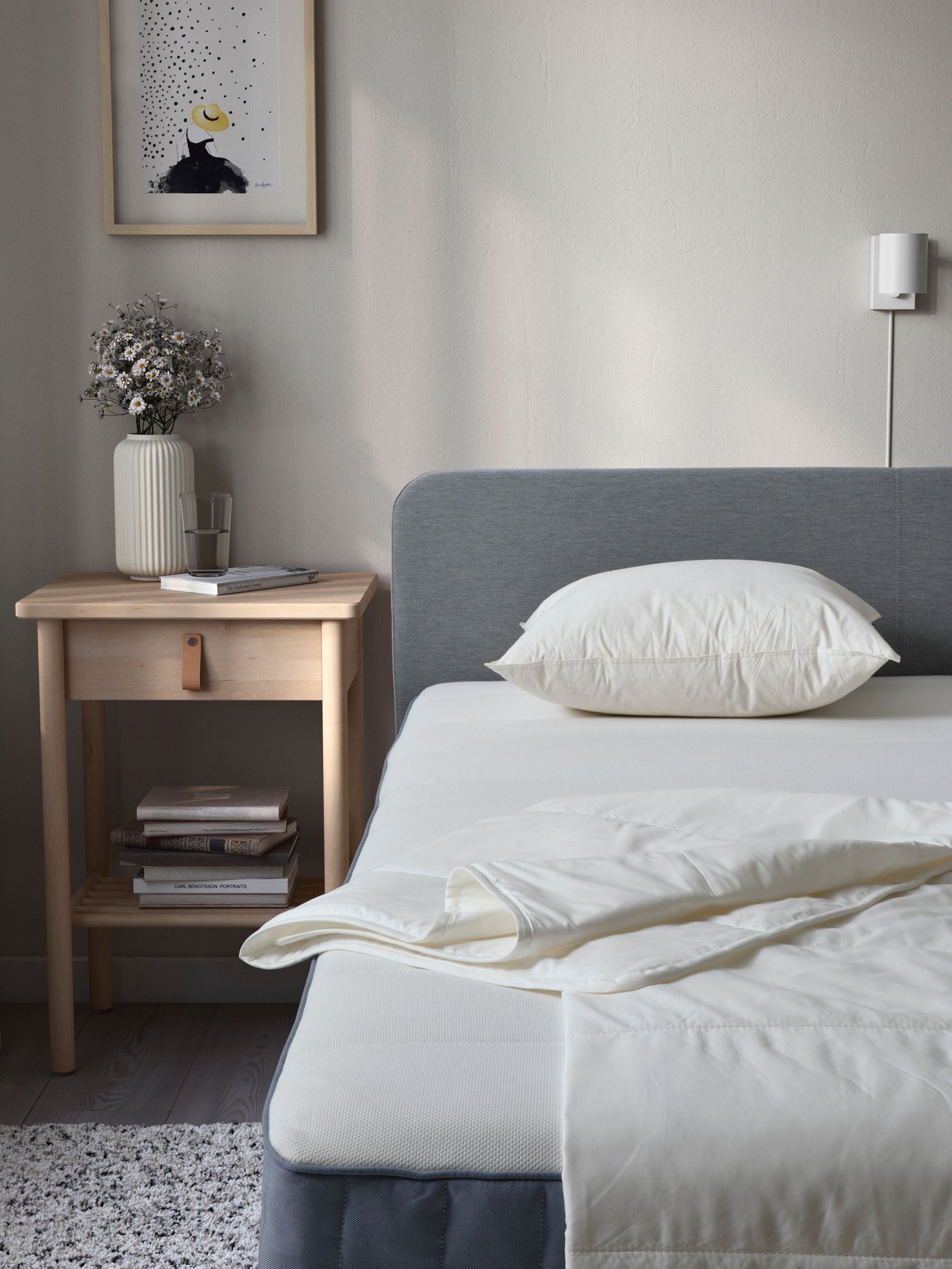 A bedroom with an upholstered bed and BJÖRKSNÄS bedside table in birch. A lightweight duvet and pillow on top of the bed.