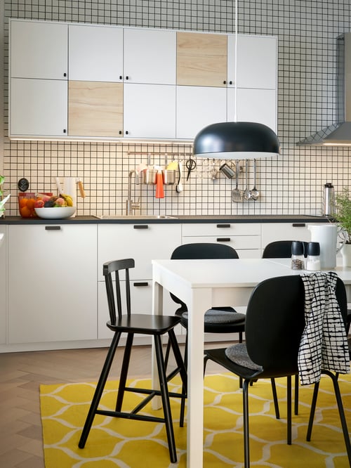 View of modern kitchen with white base cabinets, a black worktop, and extendable white table and a black junior chair.