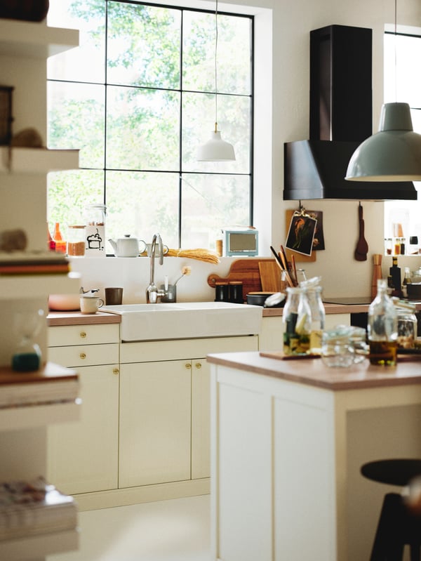 A kitchen with a kitchen island and an off/white RANARP pendant lamp above a worktop with off-white BODBYN doors below.