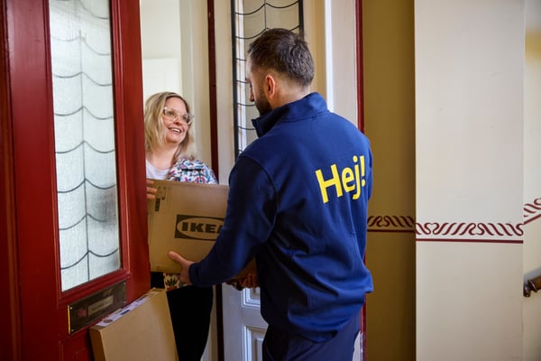 Pracownik IKEA przekazujący przesyłkę do kobiety przed jej mieszkaniem