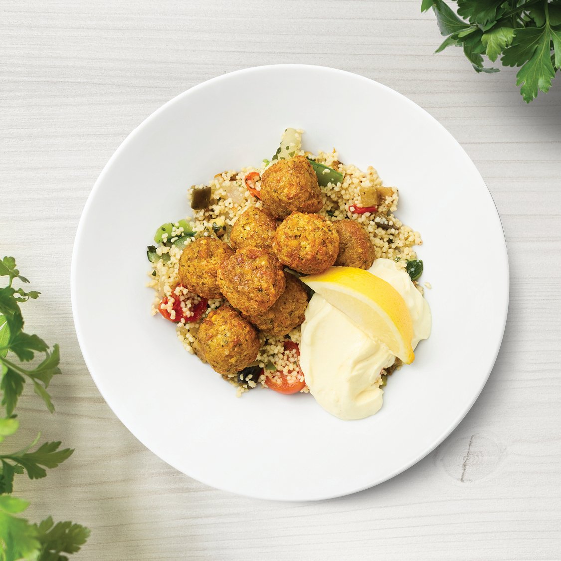 Falafel mit Gemüsecouscous und Aioli Sauce auf einem weißen Teller präsentiert