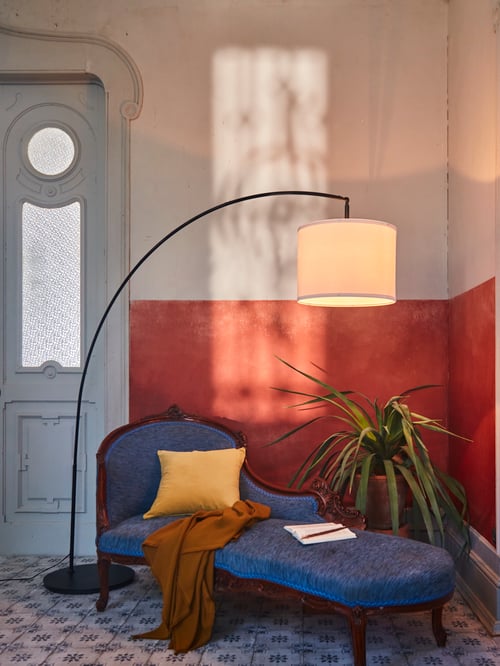 Salon moderne avec base de lampadaire arquée, abat-jour blanc, housse de coussin jaune et jeté brun.