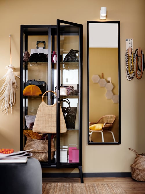 Wohnzimmer mit einer MILSBO Vitrine, einem NISSEDAL Spiegel, FLÅDIS Korb und einer NYMÅNE Wand-/Leseleuchte.